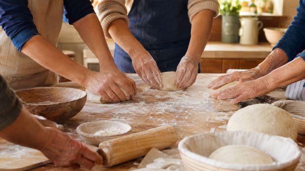Mehrere Generationen backen gemeinsam am Holztisch und formen Teig